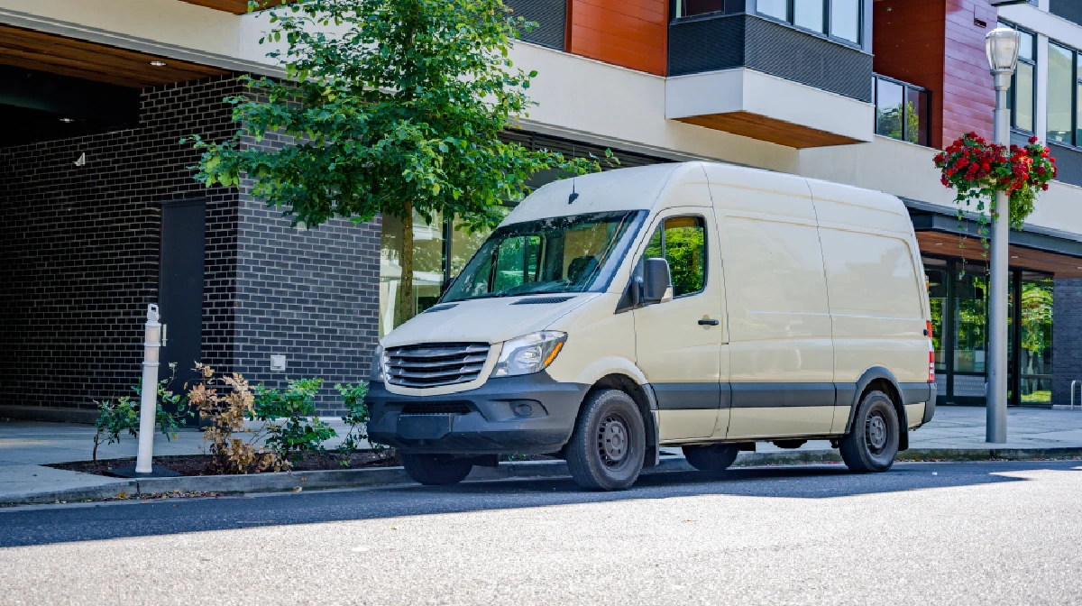 A cream-colored delivery van parked on a city street near a modern building.